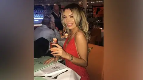 Family handout Ashley Dale, wearing a red dress, smiles as she raises a glass in a toast during a night out at a restaurant