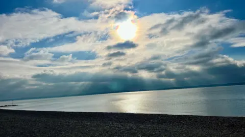 A beach scene with the sun low in the sky and the light quickly fading. There is a little blue sky but lots of cloud across the sky. The beach is empty.