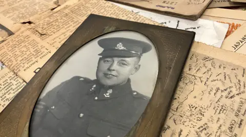 A black and white photo of Second World War solider Jack Price, in an oval wooden frame, laid on newspaper clippings from the time