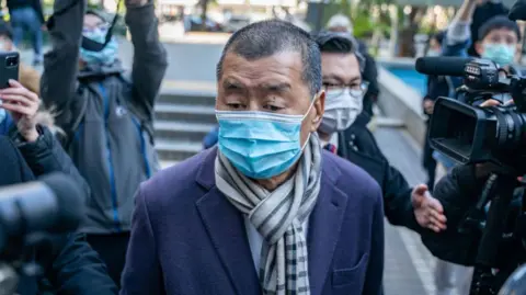 Jimmy Lai wearing a blue mask walking among a crowd