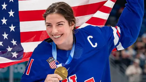 Hilary Knight smiles while holding her gold medal after the USA win women's ice hockey gold at the 2026 Winter Olympics