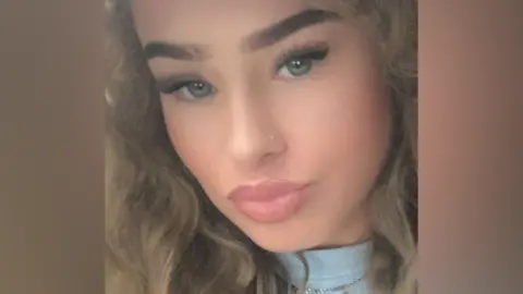 Detained in Dubai A close-up selfie of a young woman with dark blonde wavy hair, posing for the camera