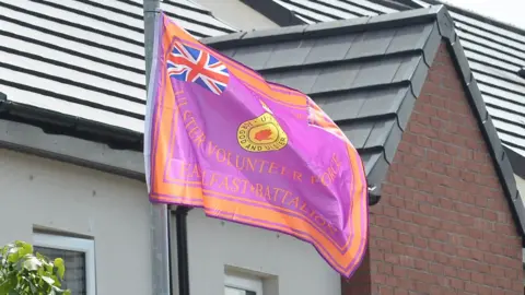 UVF flag hanging on a lamppost. There are houses behind.