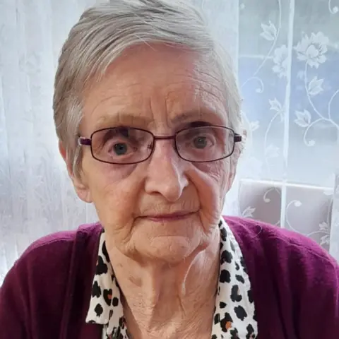 Family handout A woman with short grey hair and dark-rimmed glasses looks directly at the camera. She is wearing a purple cardigan.
