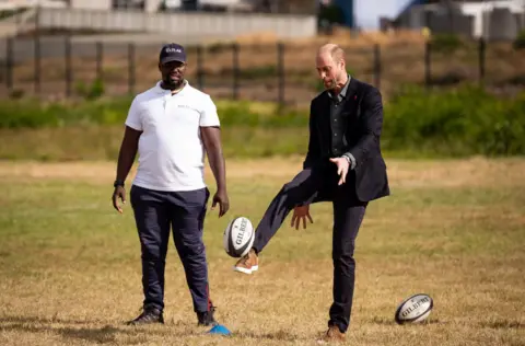 PA Media The Prince of Wales kicks a ball while taking part in a rugby coaching session with local school children during a visit to Ocean View Secondary School in Cape Town, South Africa.