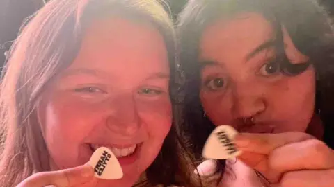 Fauve Walkerdamarell Two girls close up holding guitar pics that say Harry Styles.