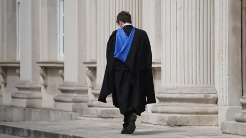 PA Media A student in a gown worn for graduations walks away from the camera with his head bowed near Senate House at Cambridge University.