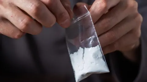 A person opens a small plastic packet of a white powder representing cocaine.