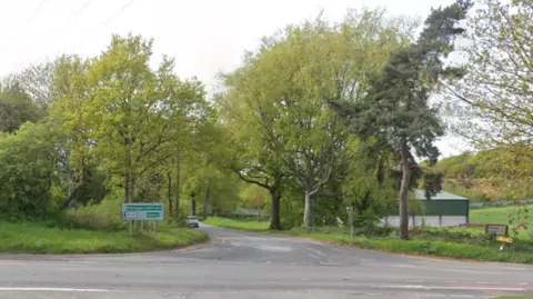 The A614 at the junction with Snape Lane. Trees line the road.