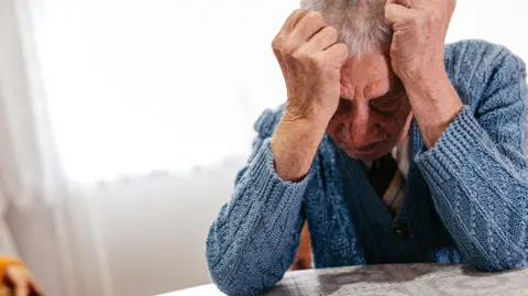 A generic image of a sad elderly man sitting with his head in his hands.