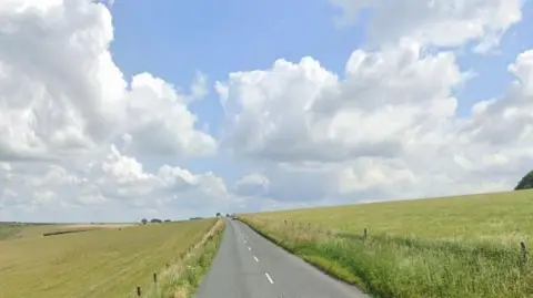 Looking down the straight road in a sunny green landscape, rolling hills on one side