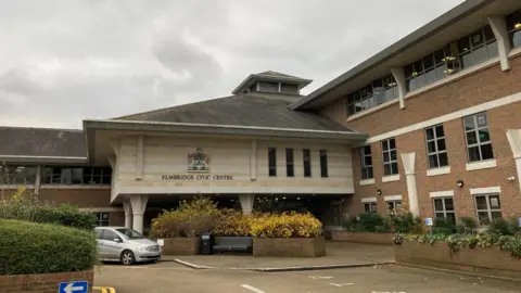 A beige and brown brick building. The building has a crest over its entrance and words reading: "ELMBRIDGE CIVIC CENTRE"