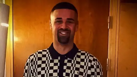 Submitted photo Tariq Evans is seen smiling at the camera wearing a black and white checked polo shirt. His black hair is short and he has a short beard and moustache.