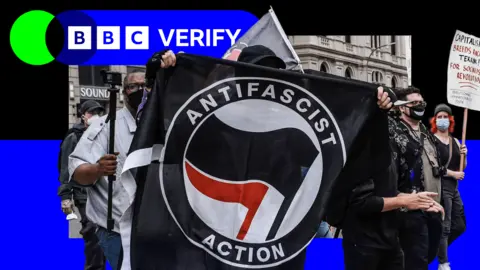 Getty Images Demonstrator macha flagą antyfa na rajdzie. Baner czyta akcję antyfaszystowską i ma czarną czerwoną flagę związaną z grupą. Inni demonstranci - niektórzy noszą maski - można również zobaczyć. 