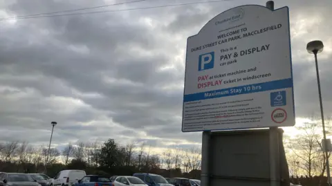 Duke Street car park in Macclesfield, Cheshire. The image shows the sign for the car park in the foreground and cars parked in the background