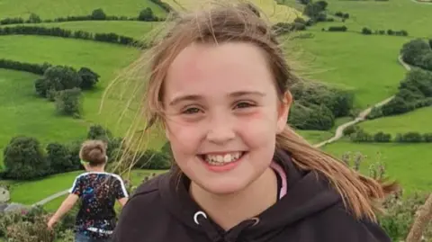 Josie Hoskins Young girl with long brown hair and black hoodie out in the countryside