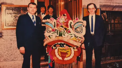 Liverpool Hung Gar Kung Fu Club Image taken outside the entrance to the Metropole Casino in 1980s with staff and Master Jimmy Chan under the lion head at a performance of the lion dance. The staff are all smiling.