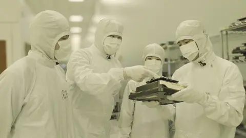 Employees of SK Hynix inspecting a chip set while dressed in white protective gear 