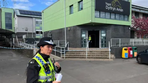 BBC A female police officer stands in front of the school