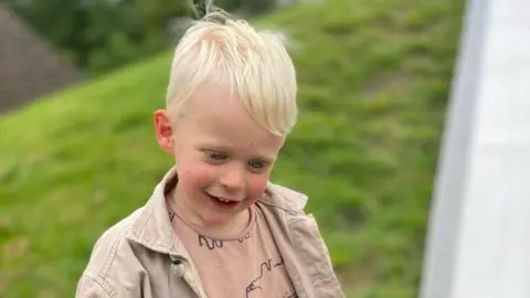 Family Handout Image of Oscar who has blonde hair and is wearing a beige jacket.