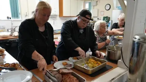 Shaun Whitmore/BBC A group of volunteers dishing up a roast dinner including meat, roast potatoes and Yorkshire puddings for people to eat.