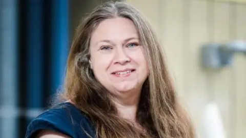University of Bradford A woman looking at the camera and smiling, she has long brown hair and is wearing a dark blue dress