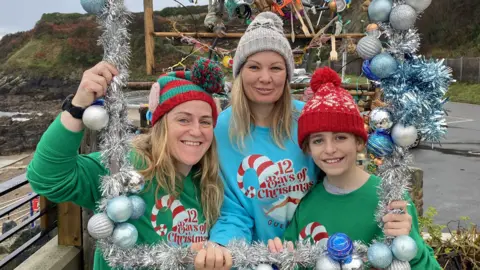 Les Bourgs Hospice three people in Christmas hats and jumpers that say 12 bays of Christmas on 