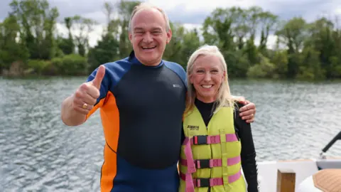 Reuters Dr Roz Savage wearing a life jacket with Sir Ed Davey wearing a wet suit in front of water 