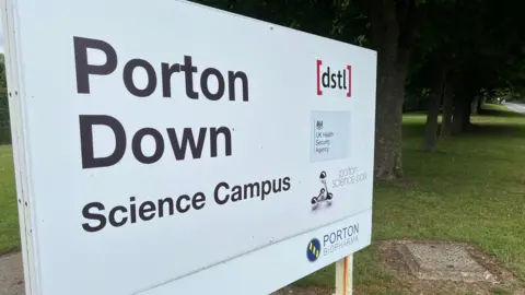 A sign with the words "Porton Down Science Campus" written on it, at the side of a road.