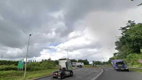 A dual carriageway with lorries driving on both sides, near to a roundabout junction