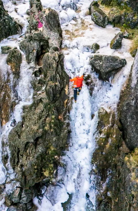 Danny Lawson/PA Wire An image of a man in bright clothing climbing up a frozen waterfall.