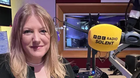 BBC Donna Jones, the police and crime commissioner wearing a black top in BBC Radio Solent Studio in front of a microphone with a yellow cover.