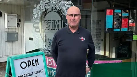 Sam Shaw A man stood outside a cafe with his hands behind his back