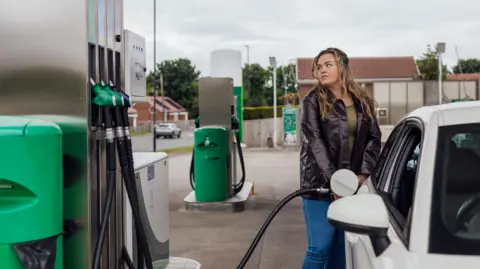 A young woman fills up her car at a petrol station