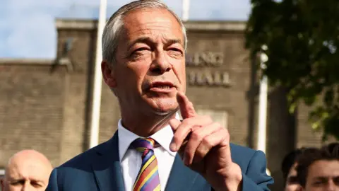 Close up of Nigel Farage talking to the press. He is wearing a blue suit and a colourful tie