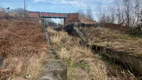 A derelict locks at Nob End on the Manchester, Bolton and Bury Canal. A channel can be seen overgrown with straw, 