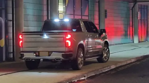 A grey pickup truck parked on a pavement. 