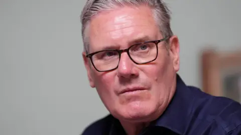 Sir Keir Starmer wearing glasses and a dark blue shirt looking serious