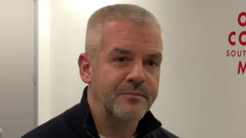 Spencer Stokes/BBC A man with very short greying hair and a salt and pepper beard.