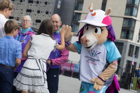 PA Media A girl with brown hair and a white polka dot dress high fives a person wearing a unicorn mascot costume