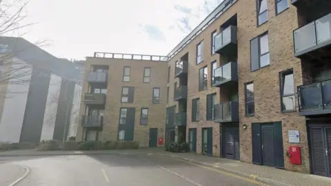 A block of flats. It is made of brown bricks with black windows. 