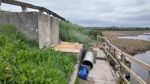 Wooden boards cover the concrete structure where contractors have installed another temporary fix to the failing tidal flap
