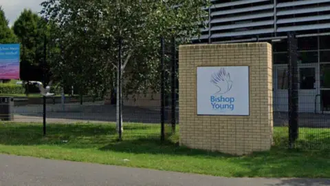 The front gates of a school. A large brick wall has a sign on it that reads 'Bishop Young'