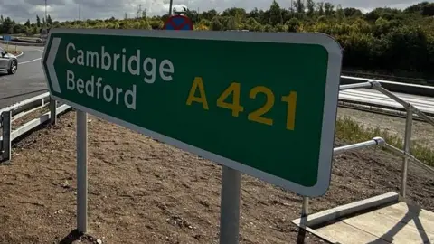 A road sign points to the direction of Cambridge and Bedford along the A421 on a bright and sunny September day