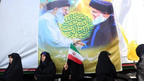 EPA Iranian women stand in front of a poster of Iranian Supreme Leader Ayatollah Ali Khamenei (L) and the late Hezbollah leader Hassan Nasrallah (R) during an anti-Israel rally in Tehran, Iran (27 September 2024)