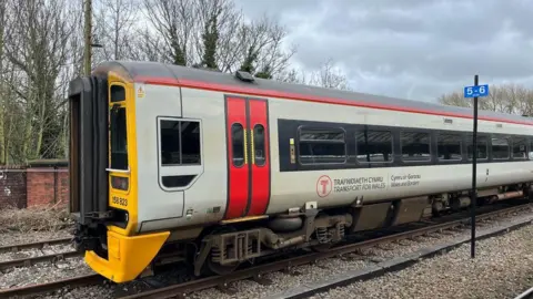 The side of a grey and red Transport for Wales train which is stopped on the racks at Shrewsbury Railway Station.