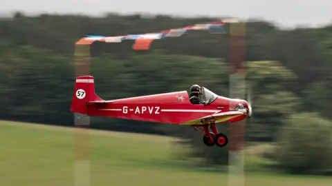 Przemek Zachwieja/European Airshows A red aircraft in the air and a pilot sat in the seat.