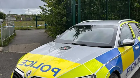a police car sits in front of police tape outside a priamry school in derry