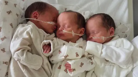 Birmingham Women's and Children's Hospital A photo of three babies with feeding tubes on their nose and wearing white onesies. 