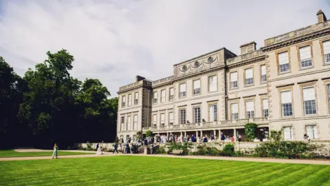 Champion News Service Ragley Hall, a large Robert Hooke Palladian mansion with party goers on the front steps and a grass lawn in front of the building. 